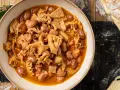 Piatto fumante di trippa alla milanese con fagioli, su un tavolo di legno rustico, accanto a pane casereccio.