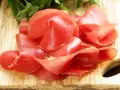 Fettine sottili di salume simile alla bresaola, rosse e lucide, disposte su un tagliere di legno con un ciuffo di prezzemolo.