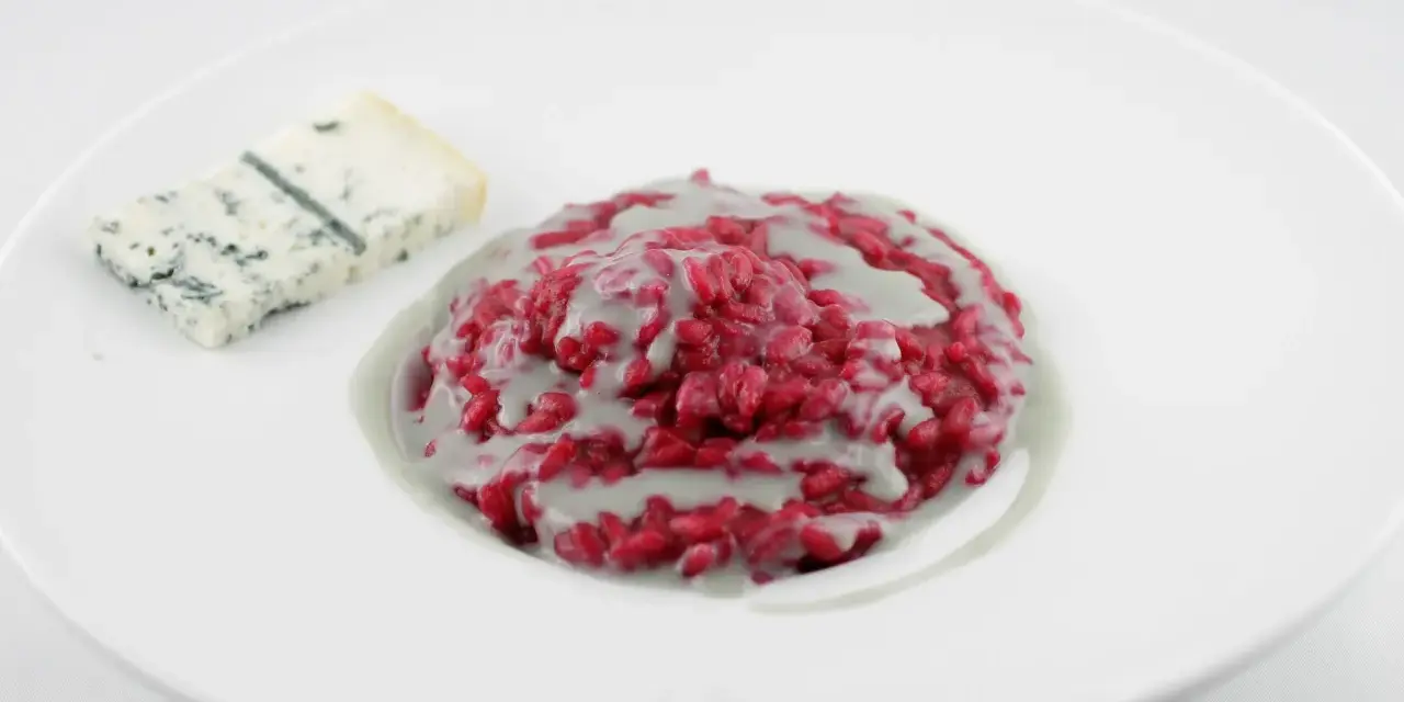 Risotto barbabietola e gorgonzola, un piatto vibrante e saporito, con una fetta di formaggio blu accanto.
