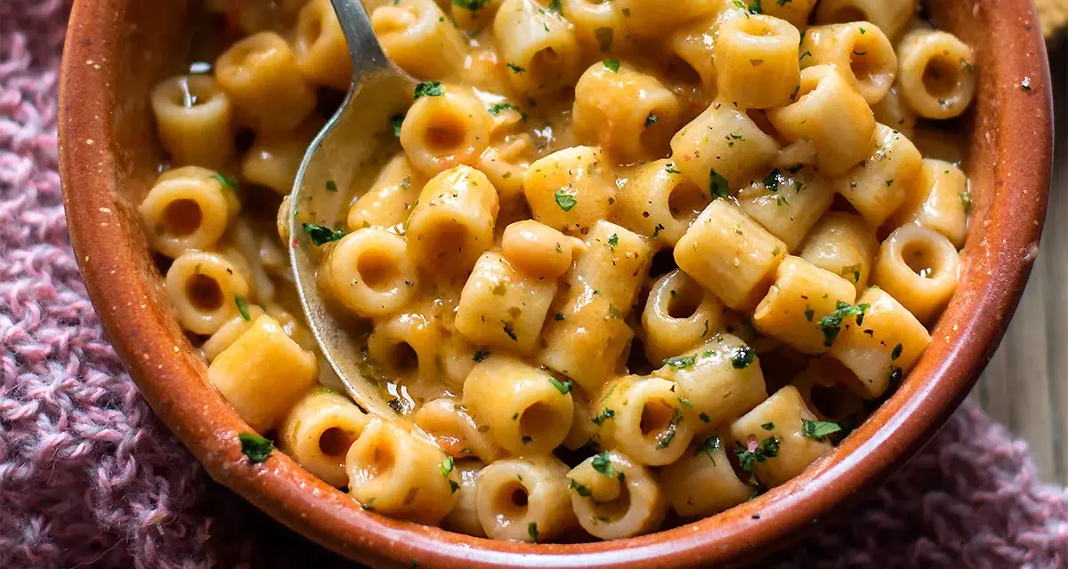 Una ciotola di terracotta piena di pasta e fagioli saporita, con un cucchiaio che ne raccoglie una porzione.