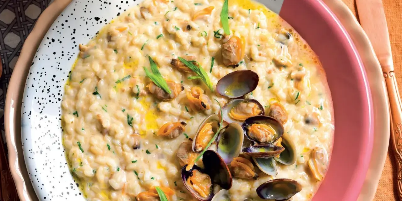 Un cremoso risotto alle vongole, guarnito con prezzemolo tritato e cozze fresche, servito in un piatto bianco a pois.