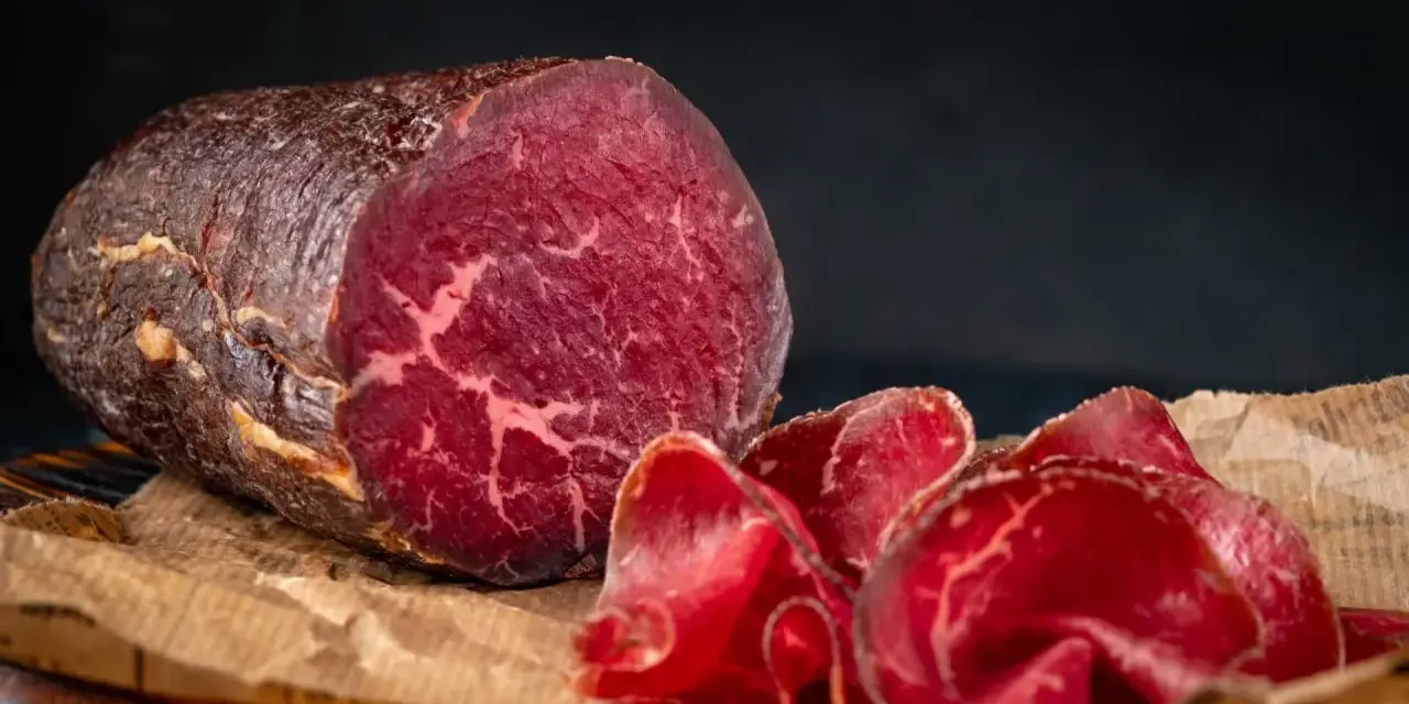 Un pezzo intero e fette sottili di bresaola, con la sua carne rossa e marezzata, evidenziano la differenza tra bresaola e punta d'anca.