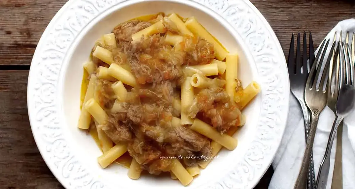Piatto di pasta con ragù genovese napoletana, servito in un piatto bianco decorato, con forchette d'argento accanto.