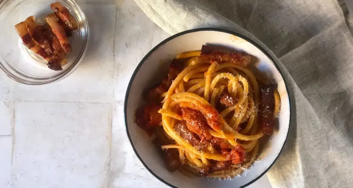 Un piatto invitante di bucatini all'amatriciana, con guanciale croccante e una salsa rossa saporita, spolverato di formaggio grattugiato.
