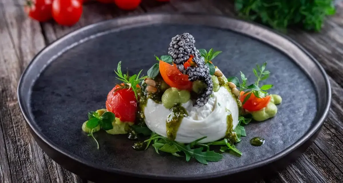 Burrata affumicata con pomodorini, crema di piselli, pinoli e pesto. Un piatto che esalta gli abbinamenti perfetti.