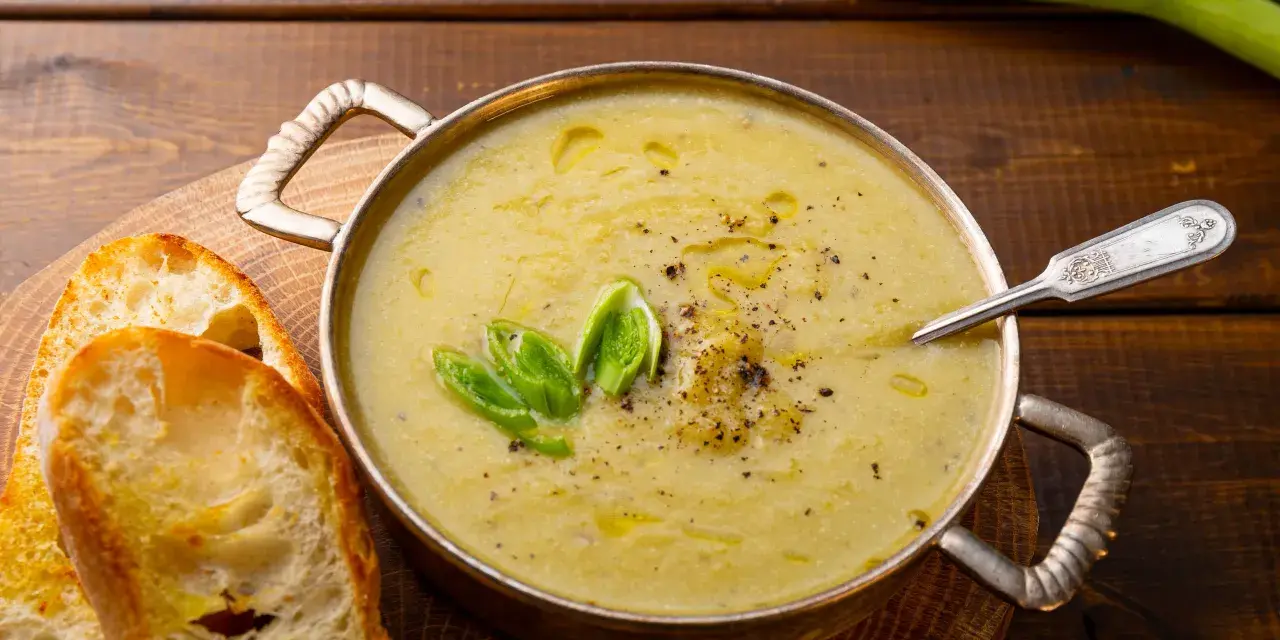 Una ciotola di calda crema di patate, guarnita con erba cipollina e pepe, servita con fette di pane tostato.