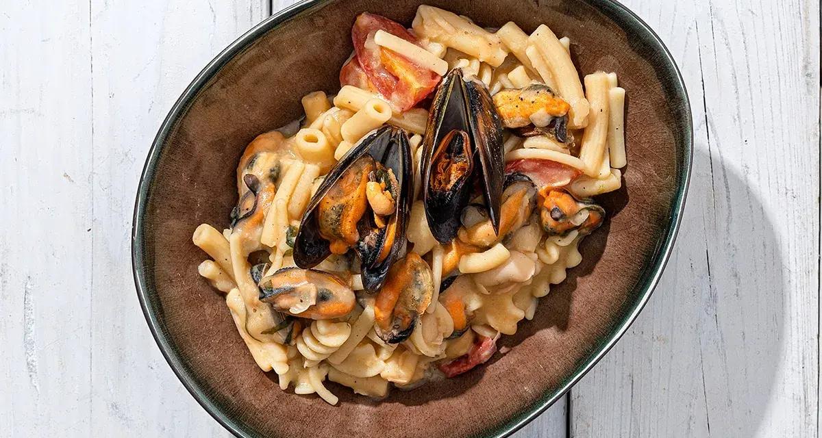 Piatto di pasta con fagioli e cozze, condita con pomodorini e una cremosa salsa.