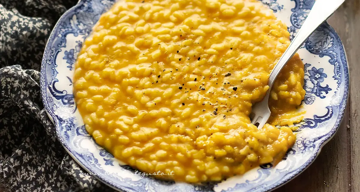 Un cremoso risotto con la zucca, servito su un piatto decorato con un motivo blu e bianco. Un cucchiaio d'argento è immerso nel piatto.
