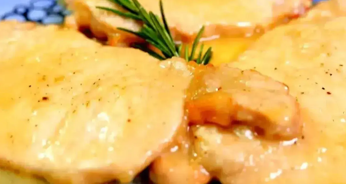 Deliziose scaloppine di maiale in salsa dorata, guarnite con un rametto di rosmarino fresco.