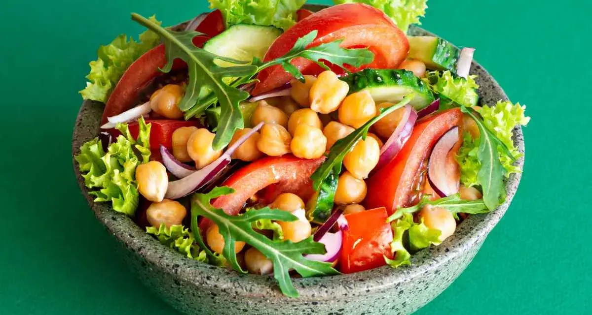 Insalata di ceci colorata con pomodori, cetrioli, cipolla rossa, lattuga e rucola in una ciotola grigia.