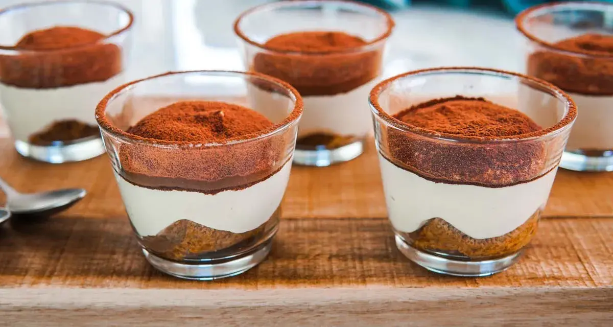 Delizioso tiramisù con pavesini senza uova, servito in bicchierini trasparenti e spolverato di cacao.