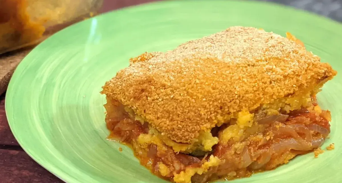 Una fetta di pitta di patate dorata e croccante, con un ripieno succulento di patate e pomodoro, servita su un piatto verde.