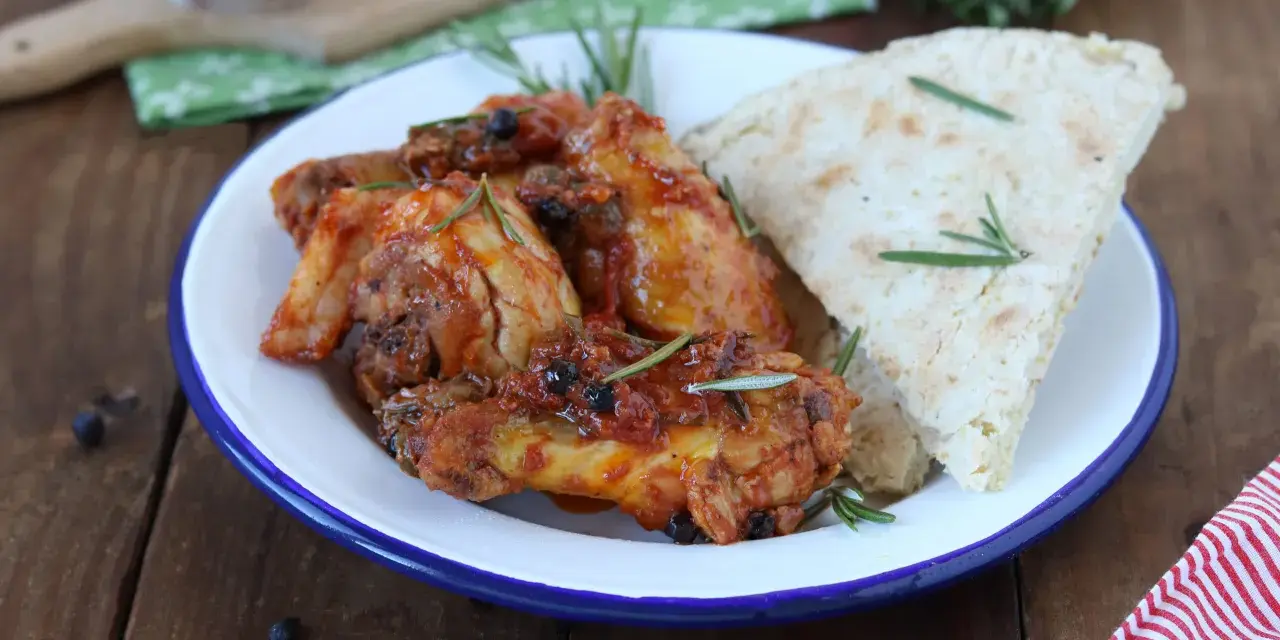 Piatto di friccò di pollo con pomodoro, olive e rosmarino, accompagnato da pane rustico.