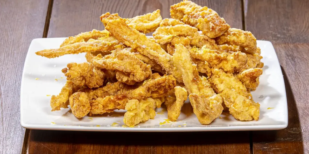 Un mucchio di croccante trippa fritta dorata, cosparsa di scorza di limone, su un piatto bianco.