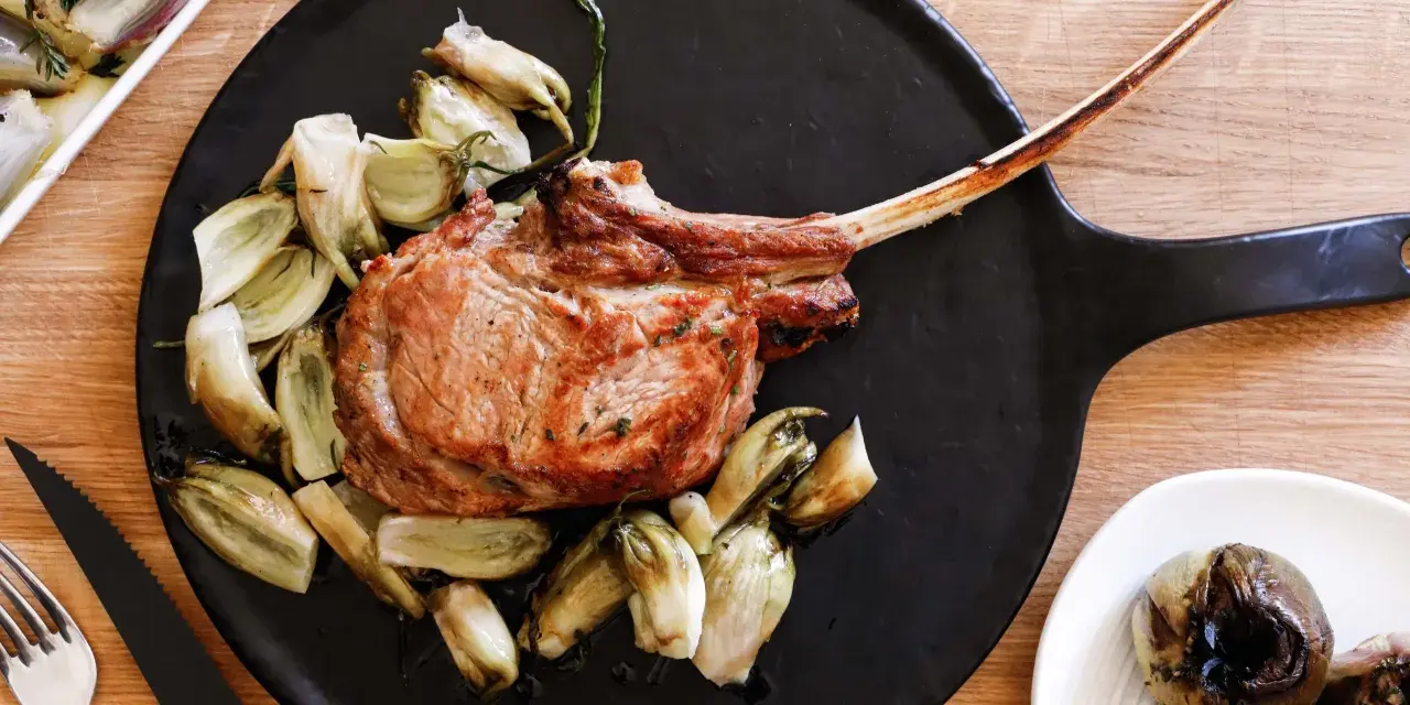 Un succulento tomahawk alla griglia, servito con verdure arrosto su un piatto nero.