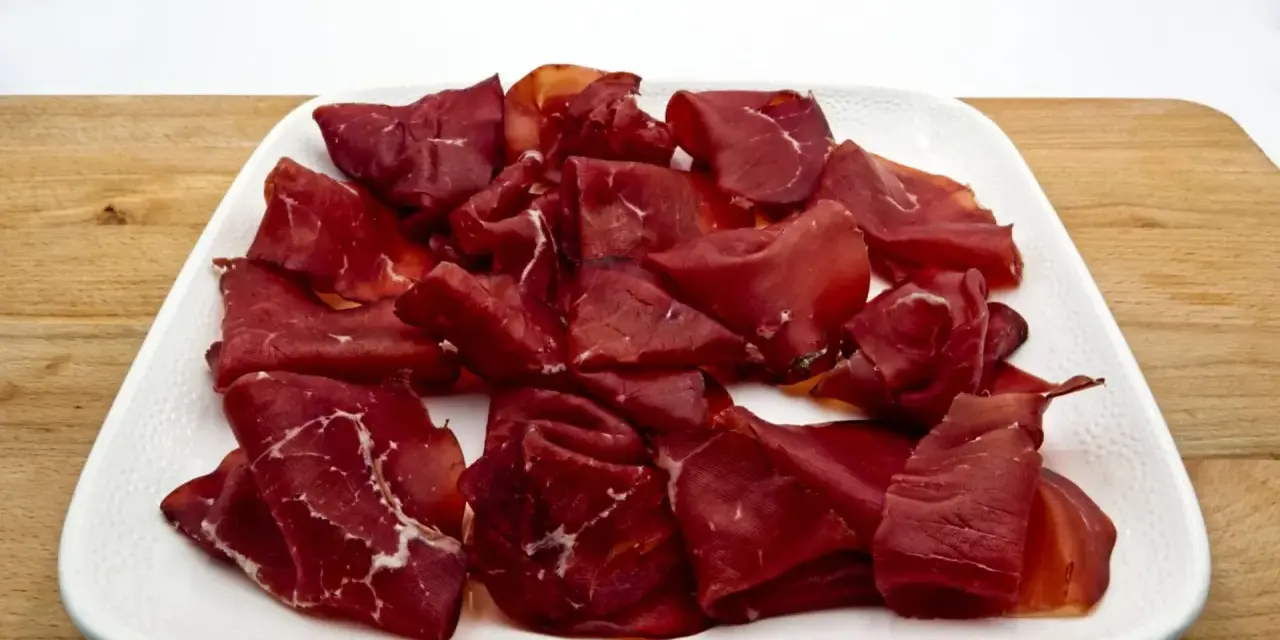 Fetta di bresaola scura, forse di cavallo, su un piatto bianco. Meglio bresaola di cavallo o manzo? La scelta è tua!