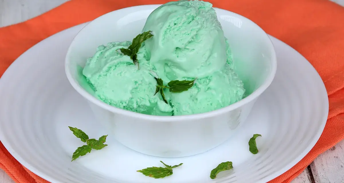 Coppa di cremoso gelato alla menta con latte condensato, guarnito con foglie di menta fresca.