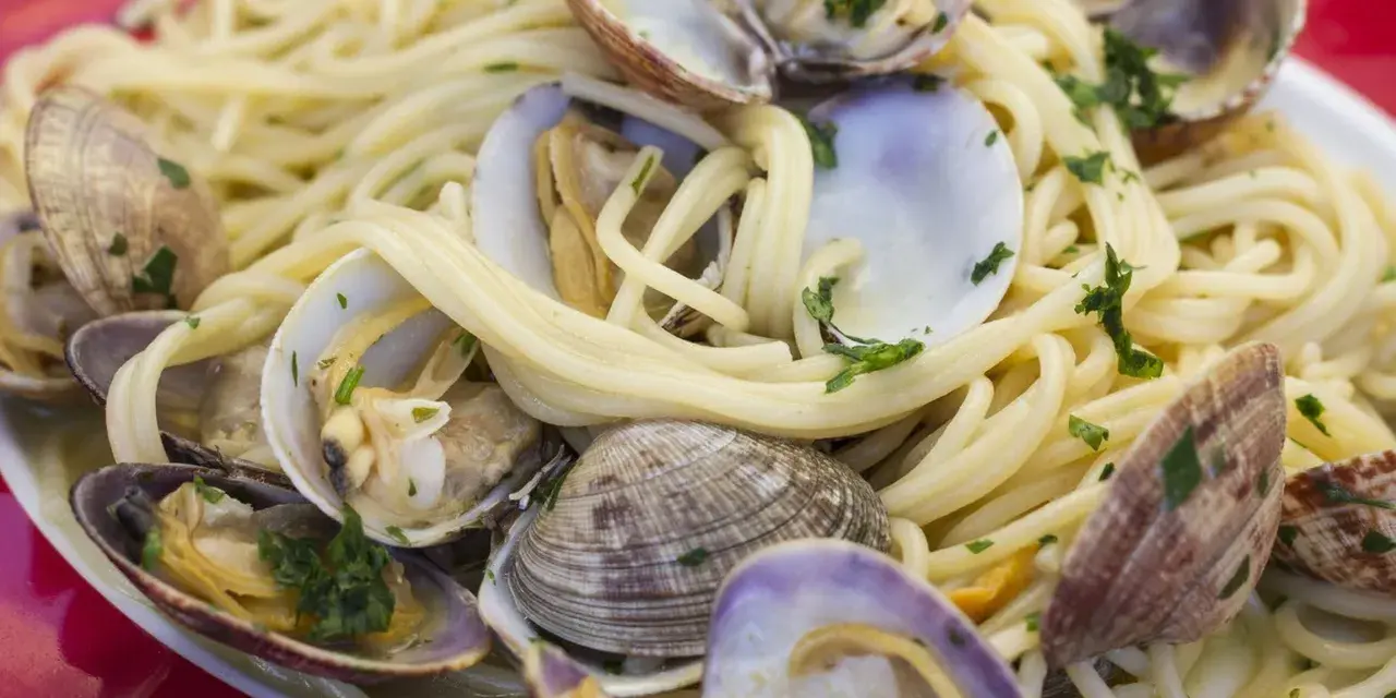 Un piatto invitante di spaghetti alle vongole, con pasta dorata e molluschi freschi guarniti da prezzemolo tritato.