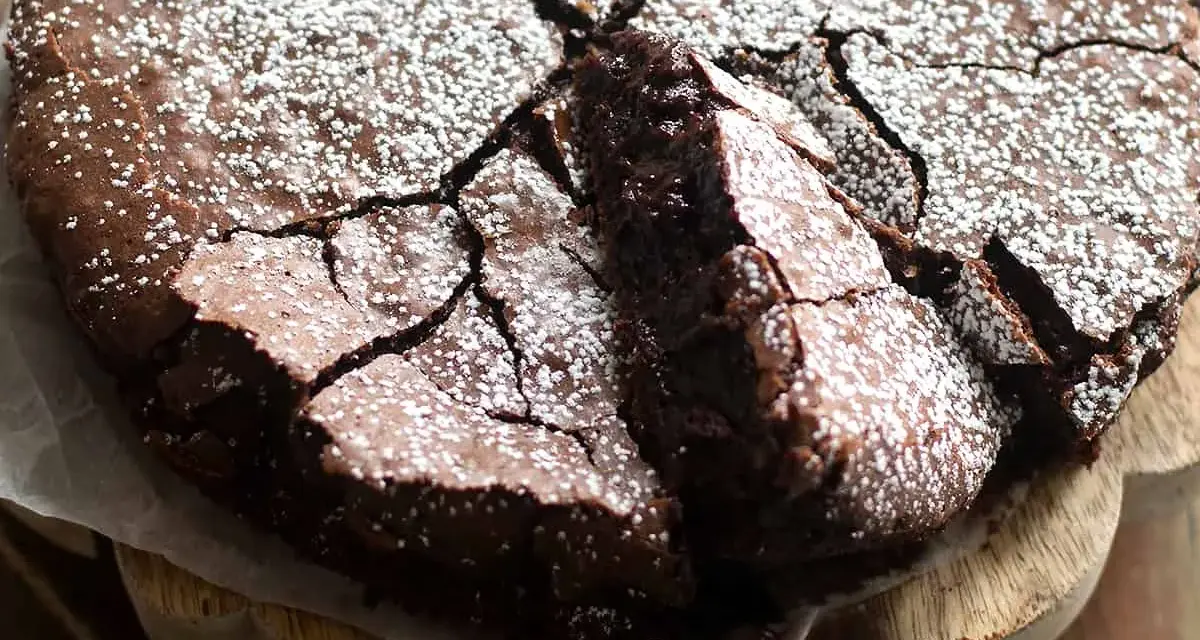 Torta fondente al cioccolato, con una crosta screpolata e cosparsa di zucchero a velo, pronta per essere gustata.