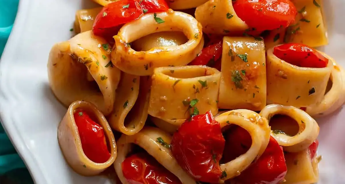 Un piatto invitante di pasta calamarata con pomodorini freschi e prezzemolo tritato, pronto per essere gustato.