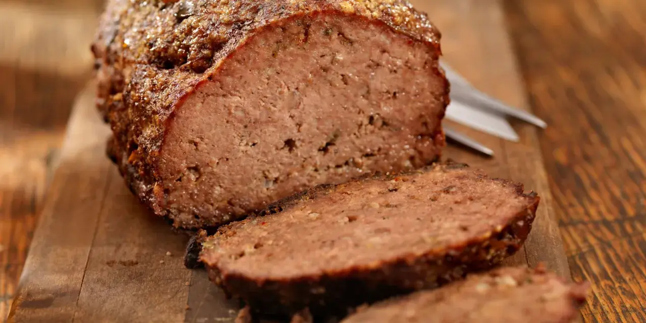 Un succulento polpettone al forno, tagliato a fette su un tagliere di legno, pronto per essere gustato.