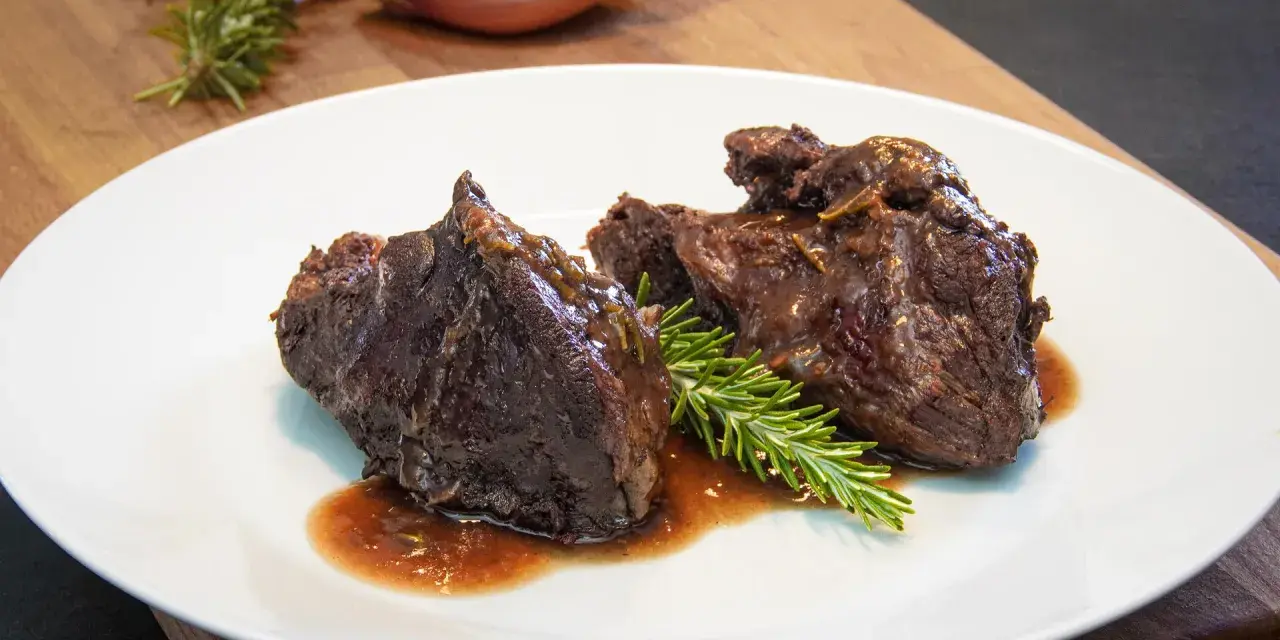 Guancia di manzo brasata, tenera e succulenta, servita su un piatto bianco con rosmarino fresco. Un piatto che fa chiedere: guancia di manzo cos'è?