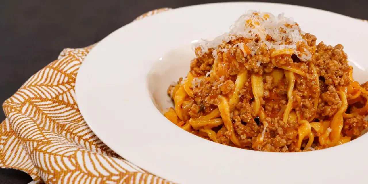 Tagliatelle ricche con sugo finto e parmigiano grattugiato, servite su un piatto bianco con tovagliolo decorato.