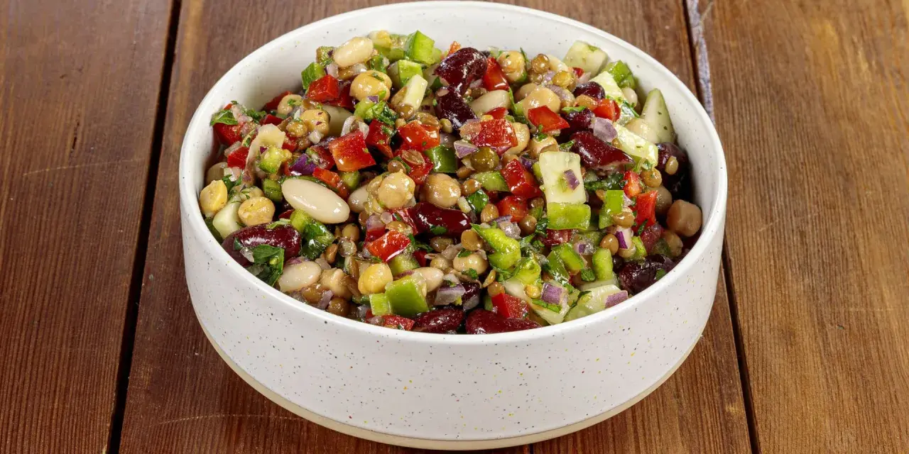 Una ciotola piena di colorata insalata di legumi, con ceci, fagioli, lenticchie, peperoni, cipolla rossa e prezzemolo fresco.