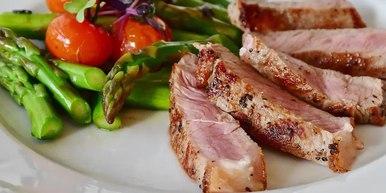 Fette di manzo magro cos'è? Succulenta carne con asparagi verdi e pomodorini su un piatto bianco.