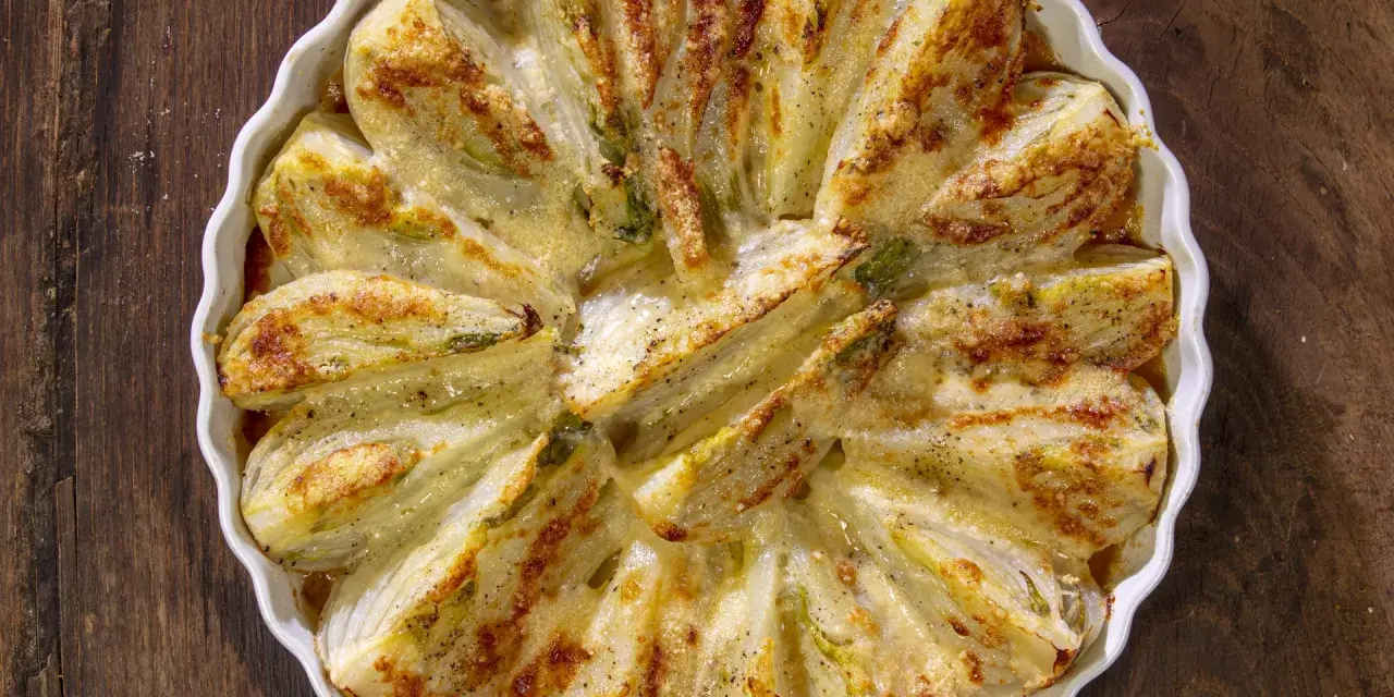 Finocchi al forno dorati e gratinati, serviti in una pirofila bianca su un tavolo di legno scuro.