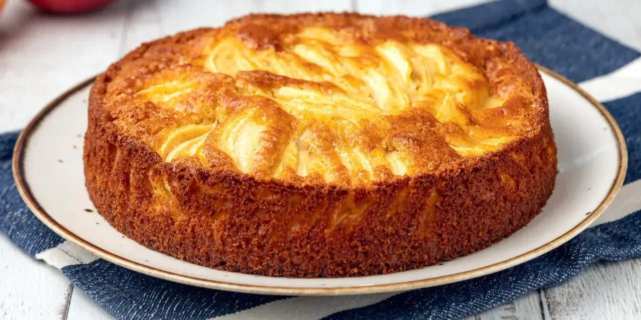 Torta di mele dorata, appena sfornata, con mele a vista. Perfetta da spennellare con un po' di sciroppo.