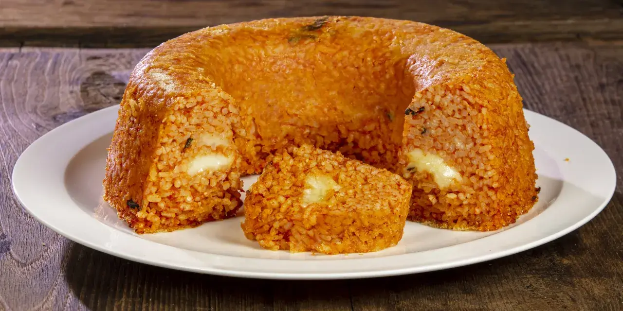 Un invitante timballo di riso, dorato e ripieno di formaggio filante, pronto per essere gustato su un piatto bianco.