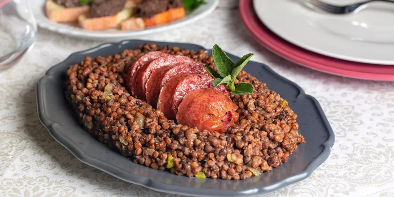 Piatto di lenticchie con fette di cotechino, un classico su come si fa il cotechino. Guarnito con salvia.