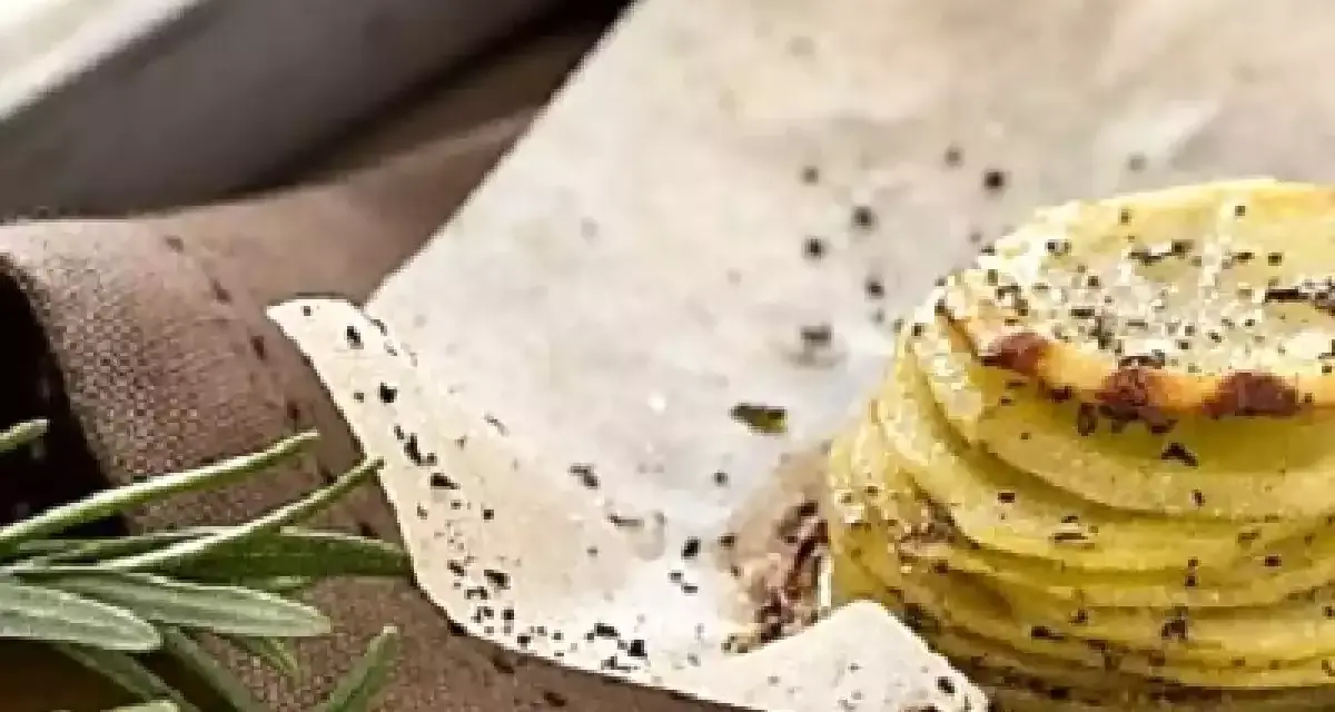 Deliziosa torretta di patate, sottili fette impilate e condite con erbe aromatiche e pepe nero, su carta da forno.