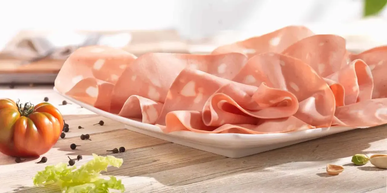 Fette di mortadella su piatto bianco, con pomodoro, lattuga e pepe. La differenza tra mortadella e bologna è nella qualità e negli ingredienti.