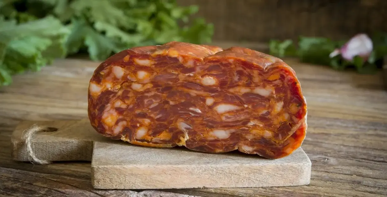 Un pezzo di salame stagionato su tagliere di legno. La differenza tra salame e sopressa è nella grana: qui si vede la carne tritata grossolanamente.