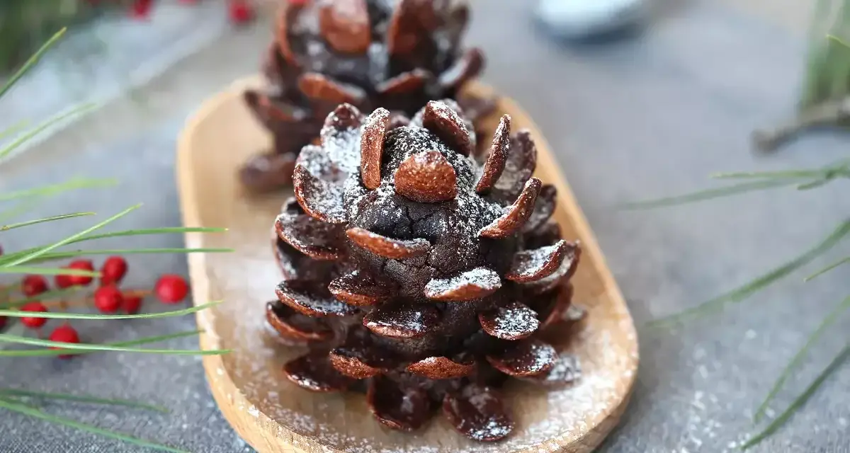 Deliziose pigne dolci decorate con zucchero a velo, su un vassoio di legno, con rami di pino e bacche rosse sullo sfondo.