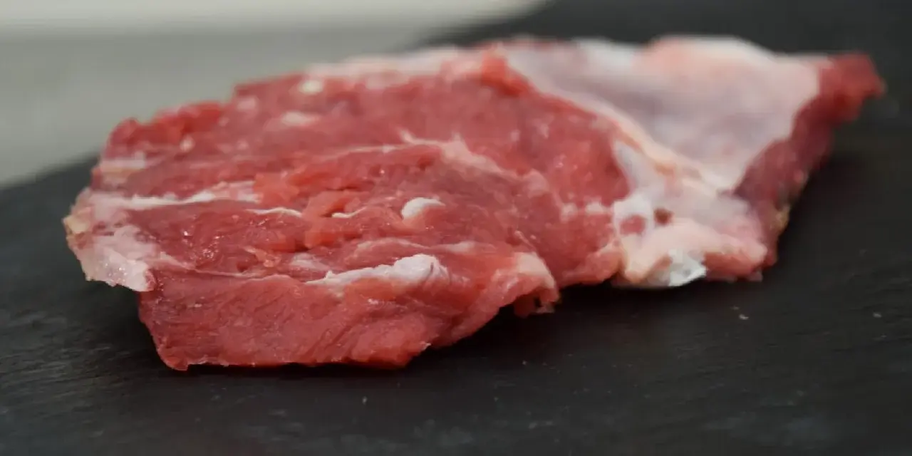 Un succulento spider steak crudo, con venature di grasso bianco, pronto per essere cucinato su una pietra scura.