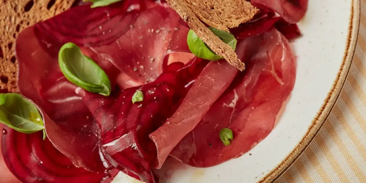 Fette di bresaola e barbabietola, esempi di salumi non insaccati quali sono, con crostini e basilico.