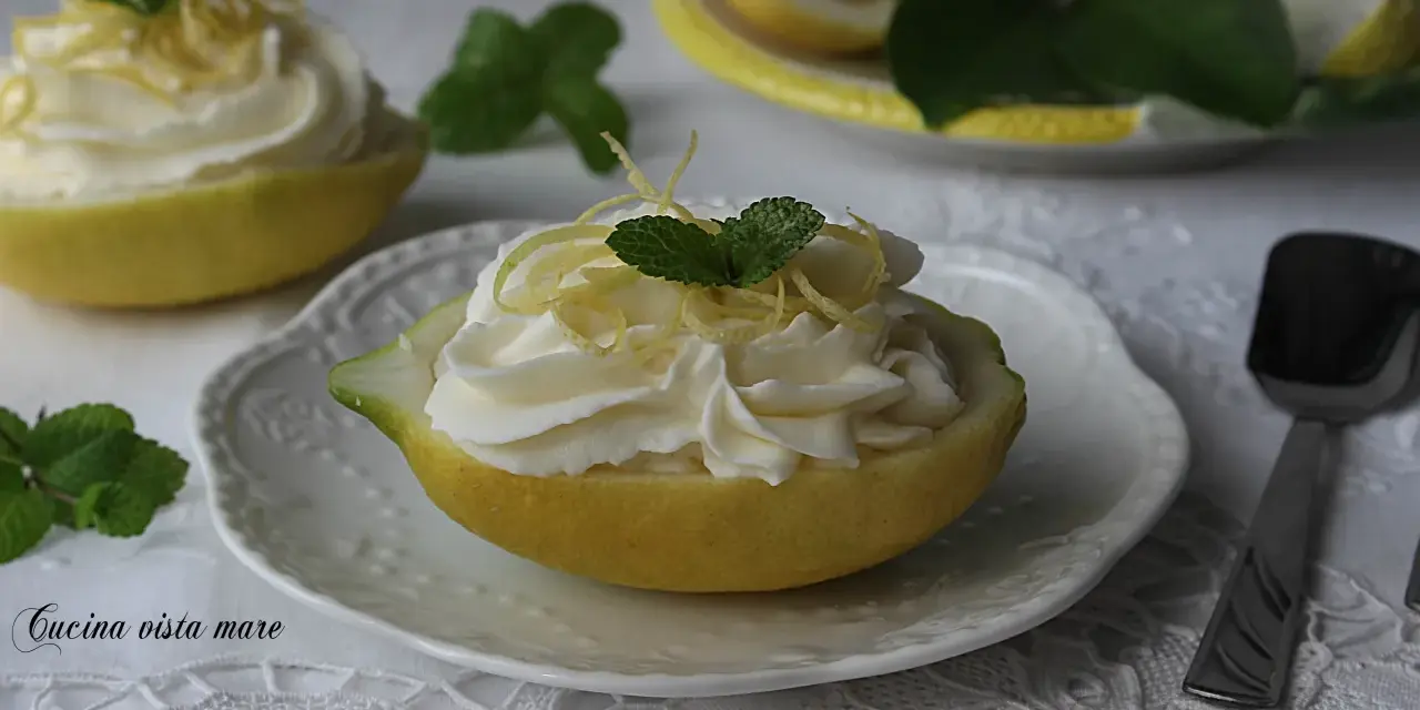 Deliziosa mousse al limone servita in un limone svuotato, guarnita con scorzette e menta.