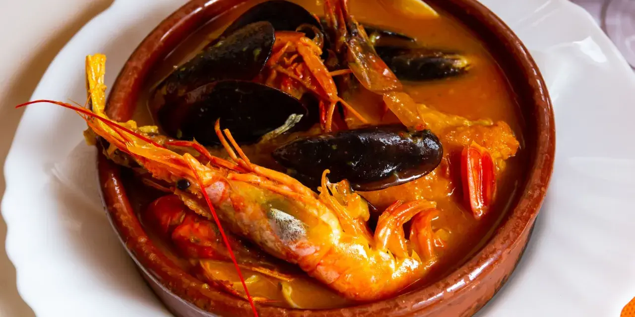 Una ricca zuppa di pesce in ciotola di terracotta, con gamberoni, cozze e pomodorini.