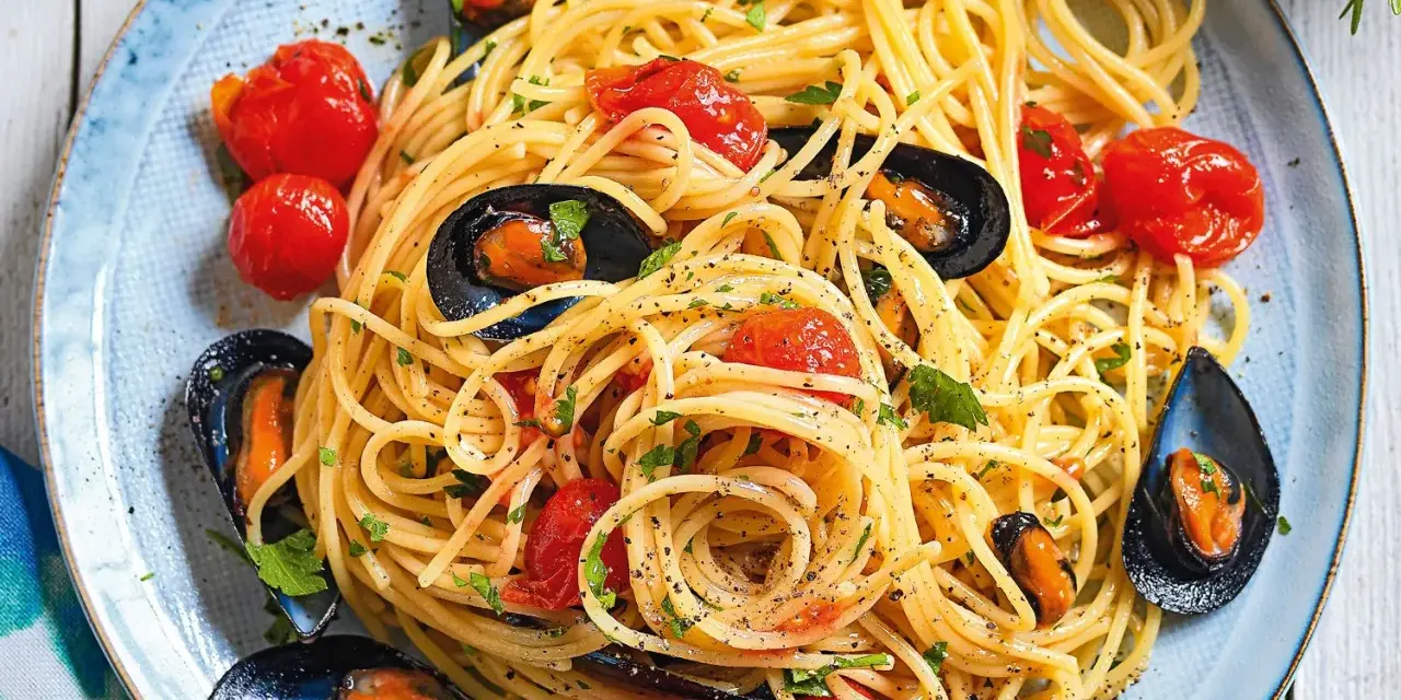 Un piatto invitante di spaghetti con le cozze e pomodorini, condito con prezzemolo fresco e pepe nero.