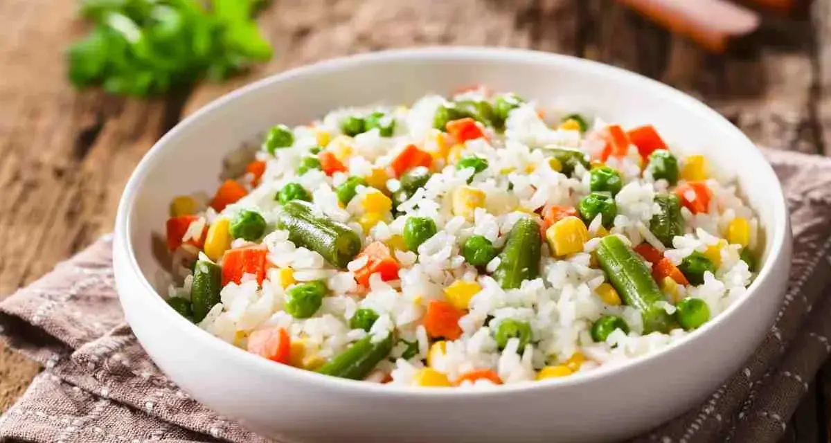 Un piatto di riso per insalata di riso, con piselli, carote, fagiolini e mais, su un tovagliolo di stoffa marrone.