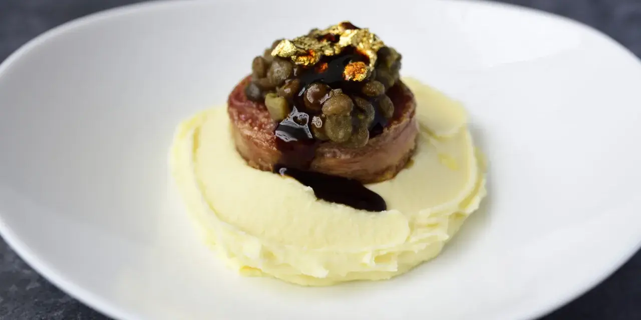 Piatto moderno con lenticchie e cotechino, un omaggio alla tradizione, servito su purè di patate e decorato con oro edule.