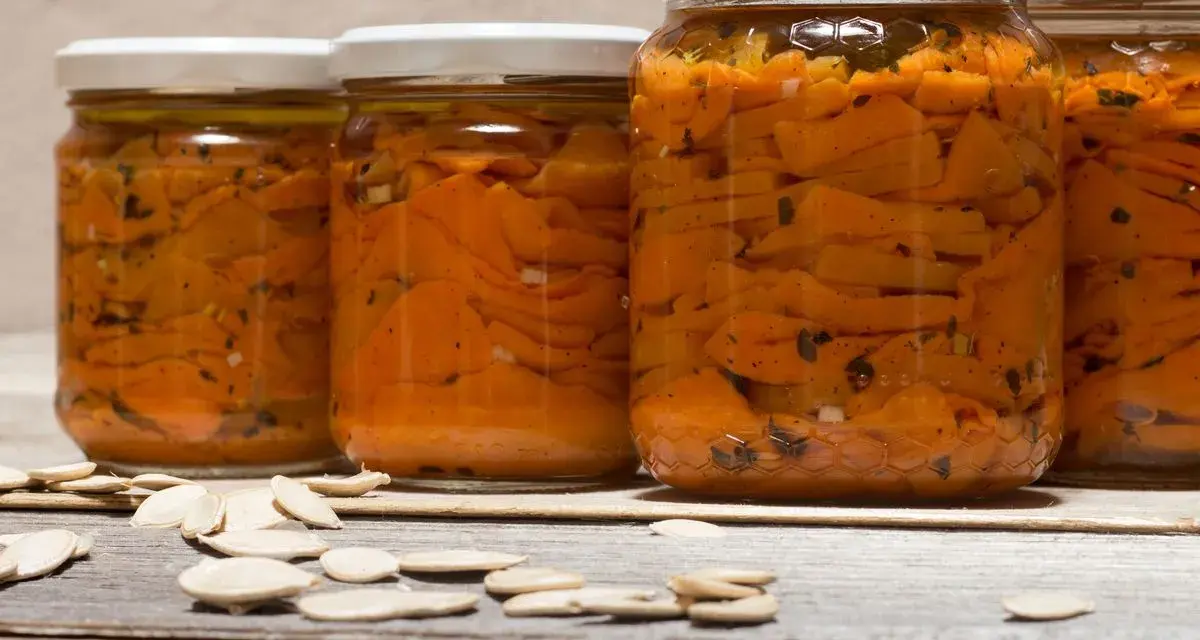 Barattoli di zucca sott'olio in agrodolce, con semi di zucca sparsi sul tavolo di legno.