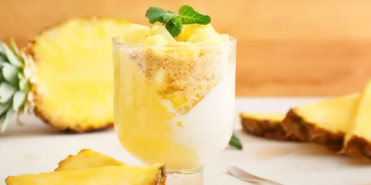 Delizioso dolce con ananas fresco, yogurt e crumble. Un bicchiere pieno di gusto tropicale, con fette di ananas e menta a guarnire.