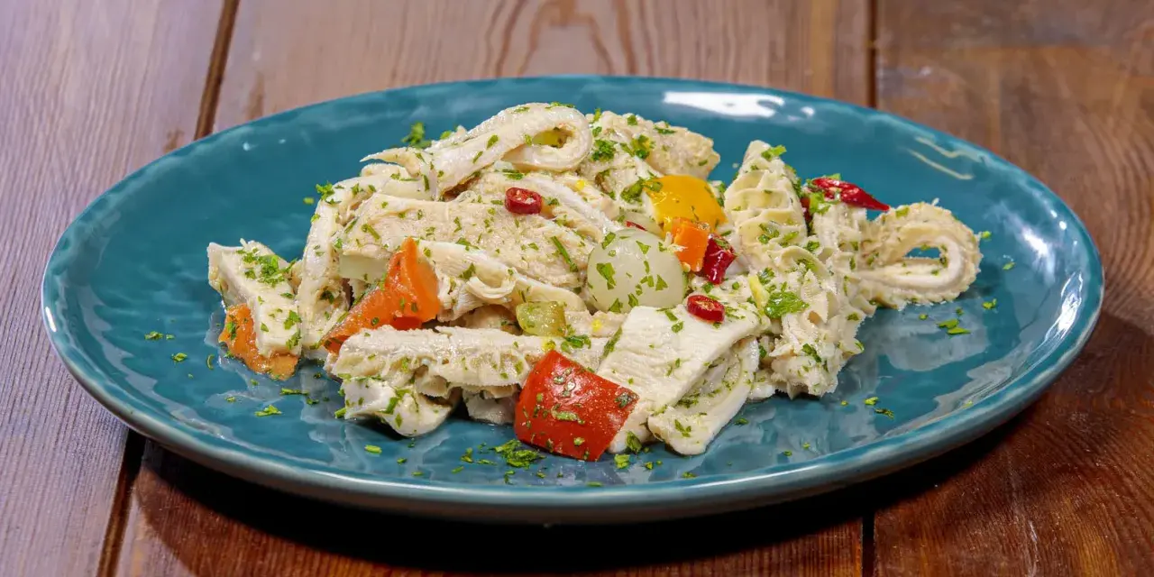 Piatto di insalata di trippa condita con erbe aromatiche, peperoncino e verdure colorate.