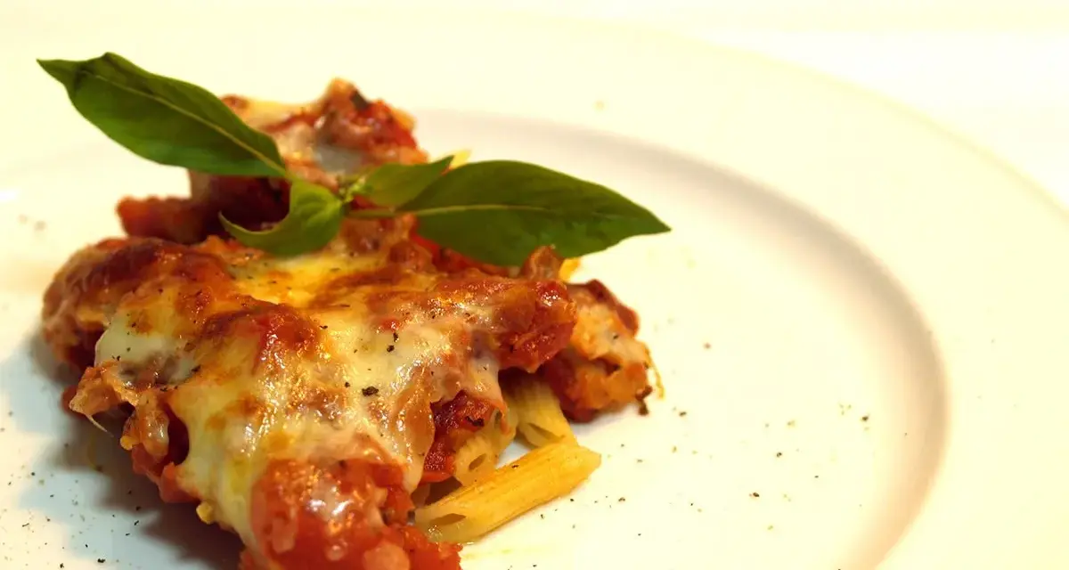 Porzione di pasta ncasciata fumante, con formaggio filante e basilico fresco, su un piatto bianco.
