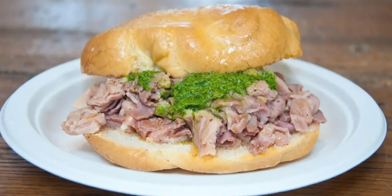 Panino con lampredotto, un classico street food fiorentino. La ricetta prevede trippa di bovino cotta e servita in un panino morbido con salsa verde.
