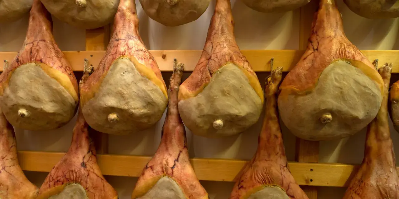 Filetti di salumi appesi a stagionare su scaffali di legno.